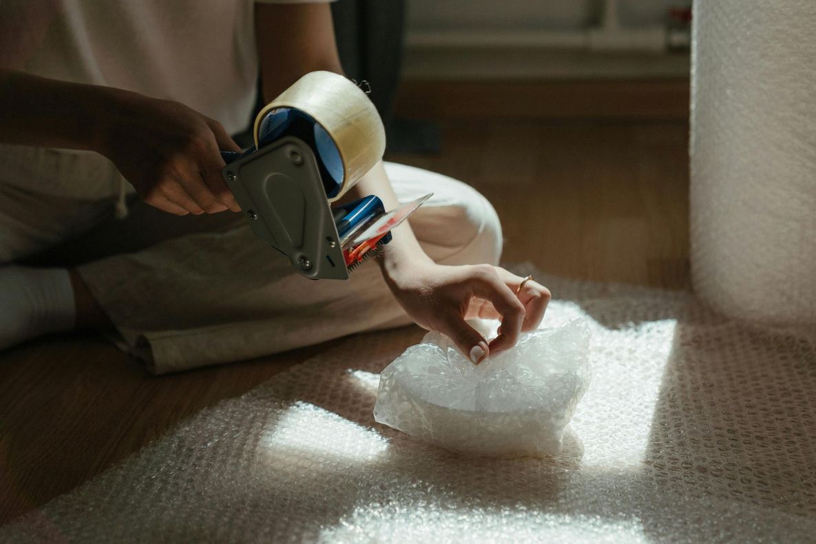 Person taping bubble wrap, packing item on a hardwood floor indoors.