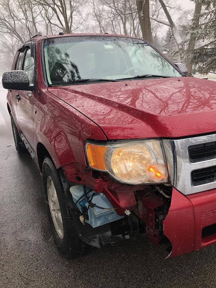 A red ford escape with a damaged front end is parked on the side of the road.
