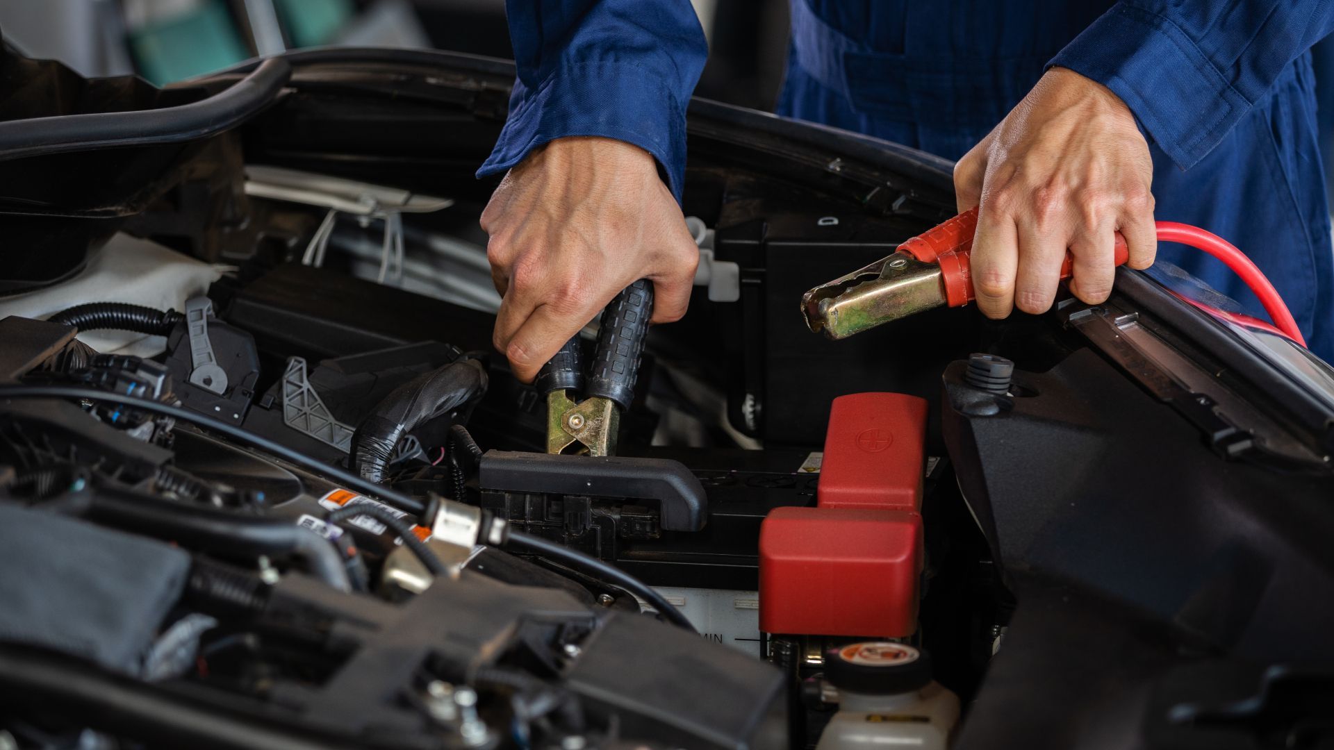 A mechanic is charging a car battery with a jump starter.