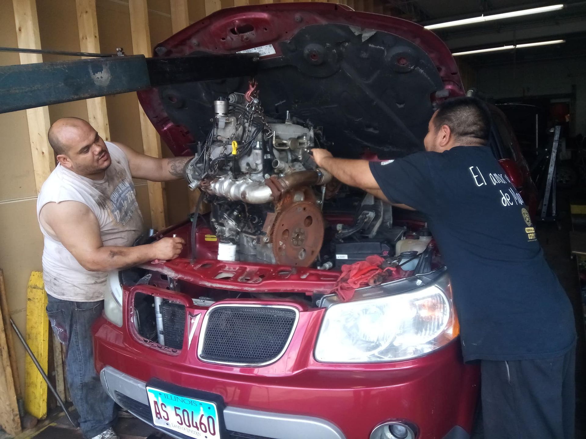 Two men are working on the engine of a red car.