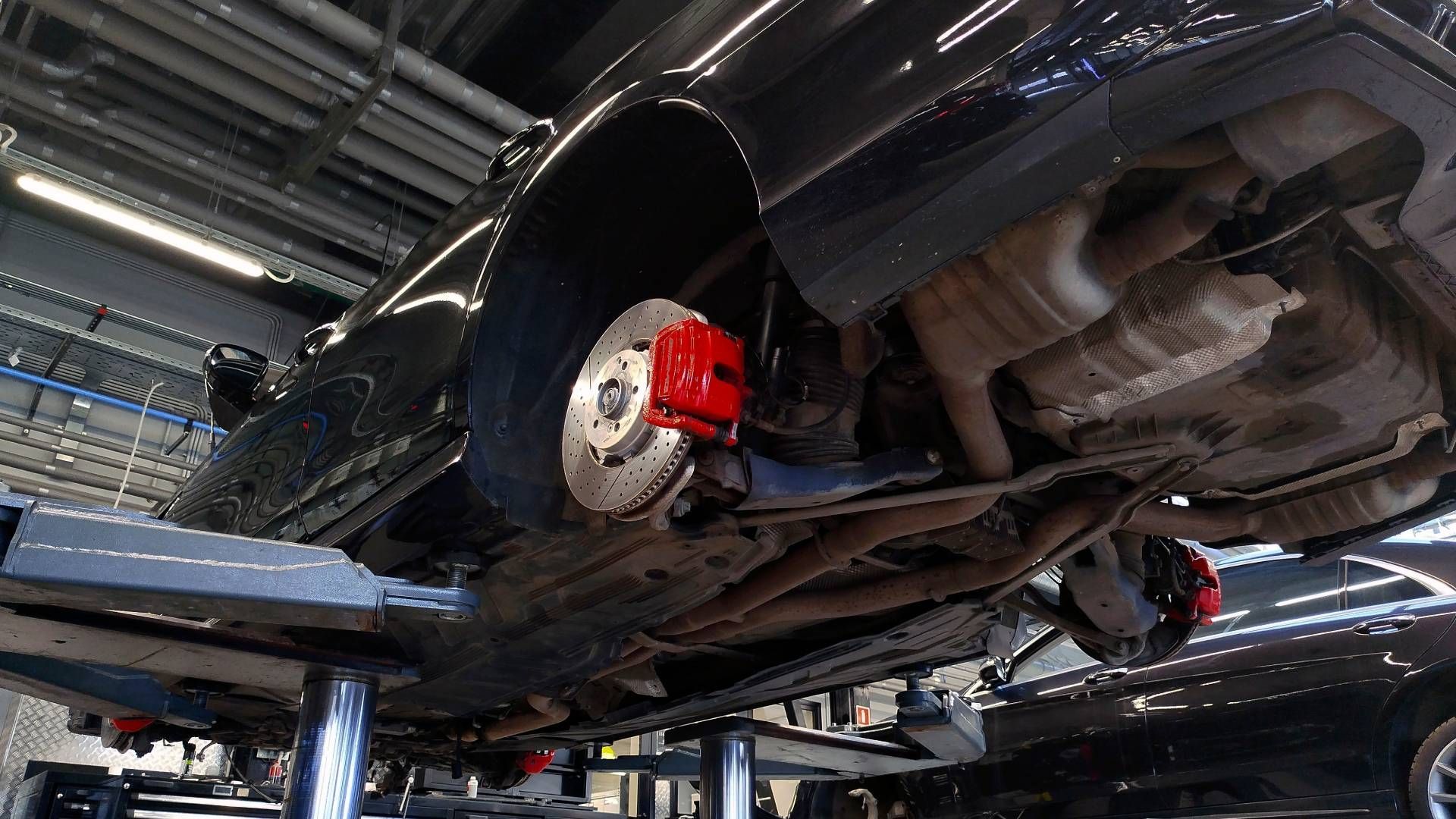 A black car with red brake calipers is sitting on a lift in a garage.