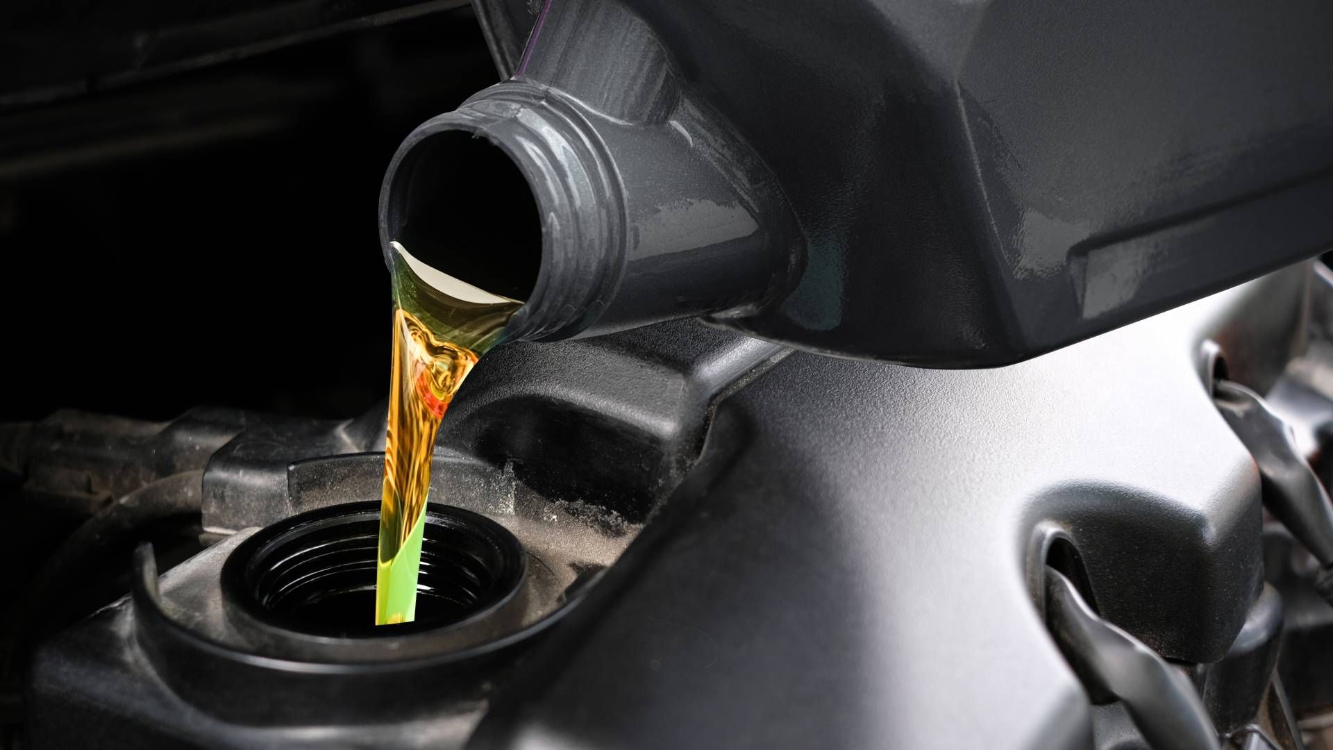 A close up of a person pouring oil into a car engine.