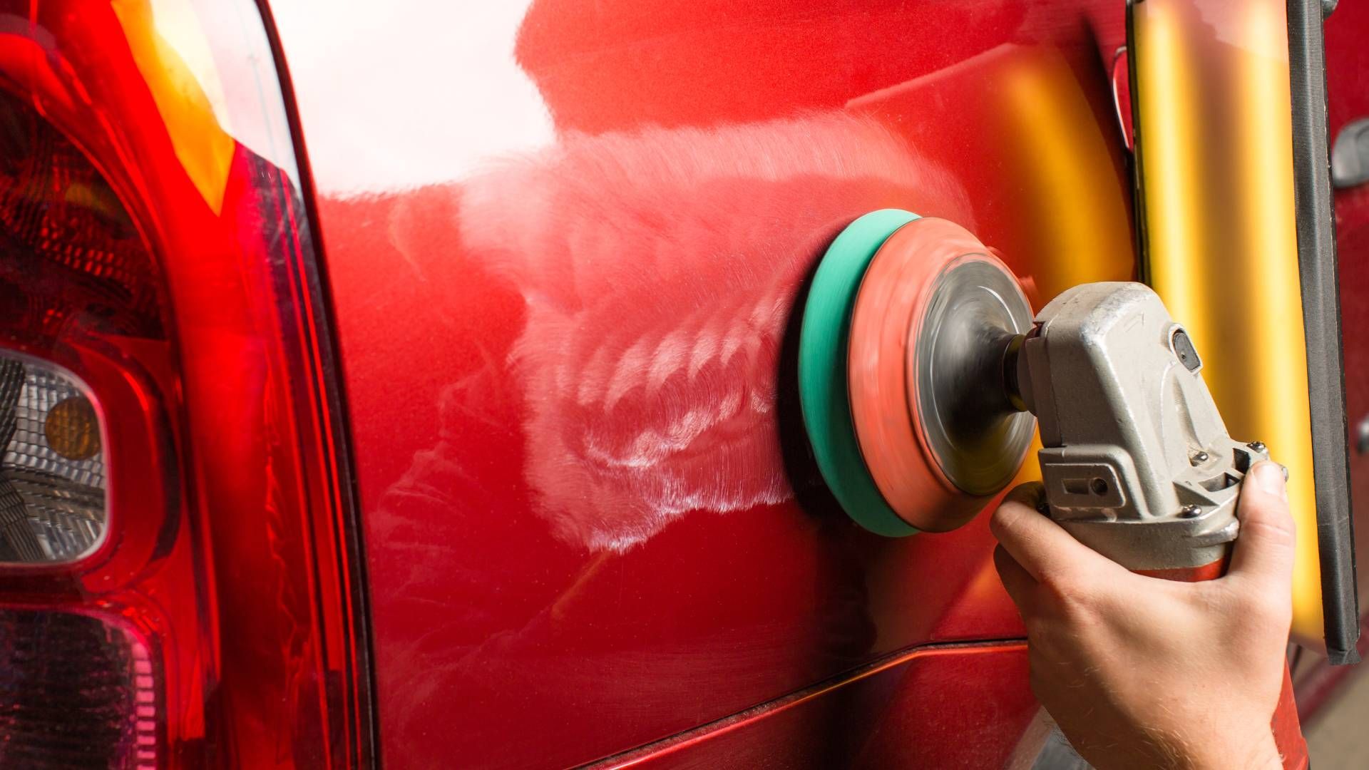 A person is polishing a red car with a machine.