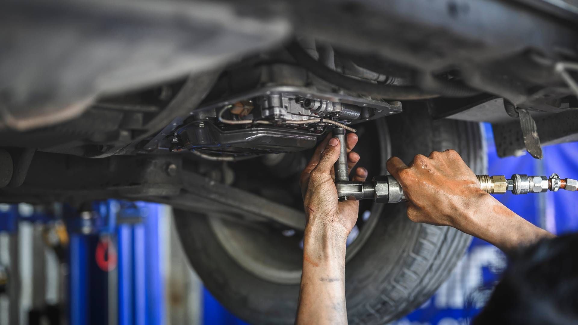 A man is working on the underside of a car in a garage.