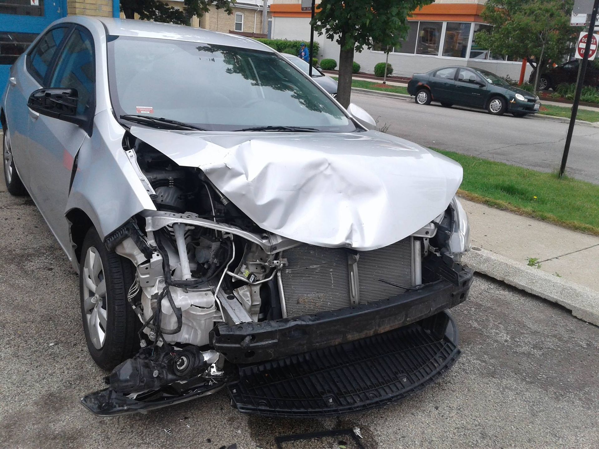 A damaged silver car is parked on the side of the road