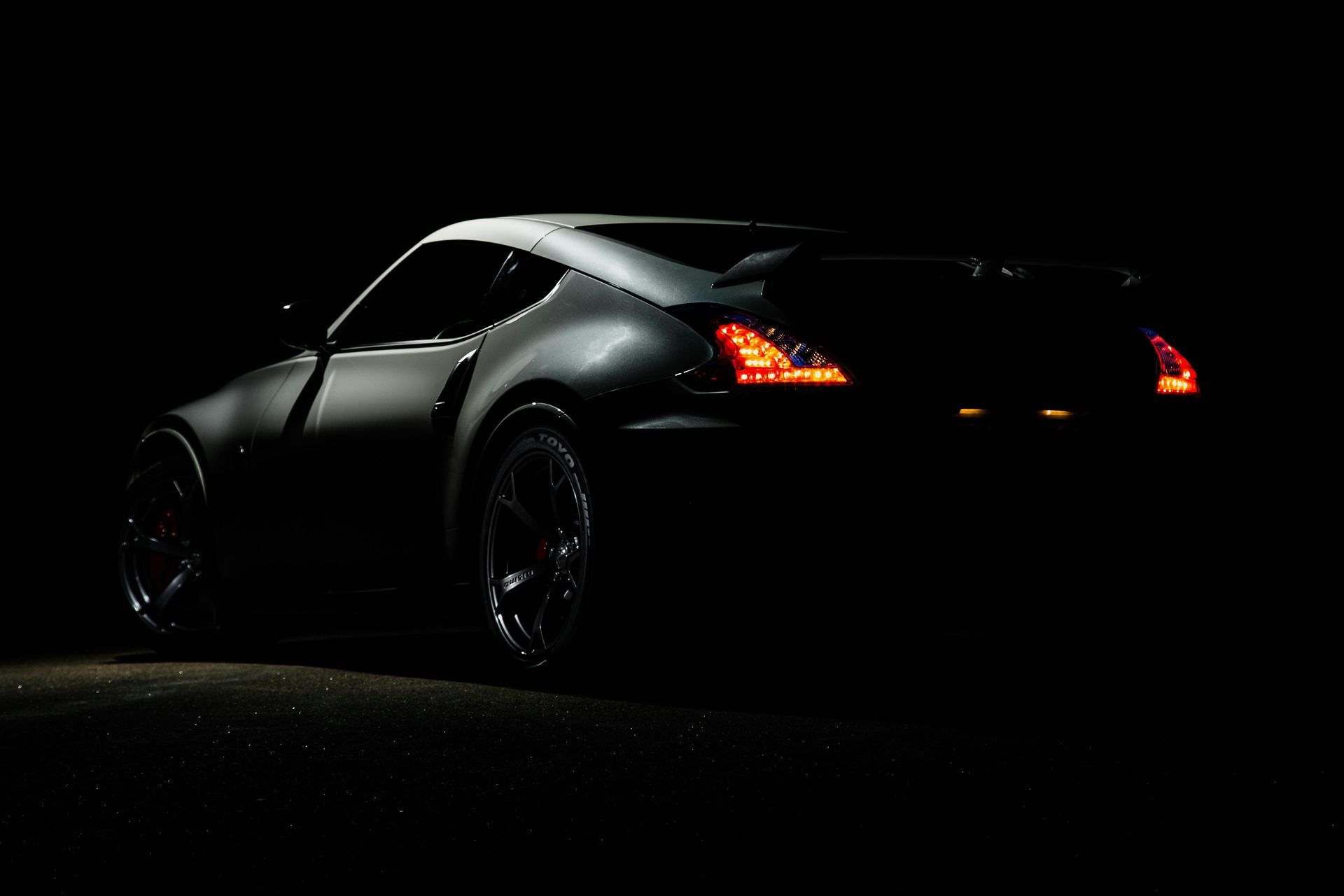 A black sports car is parked in the dark with its lights on.