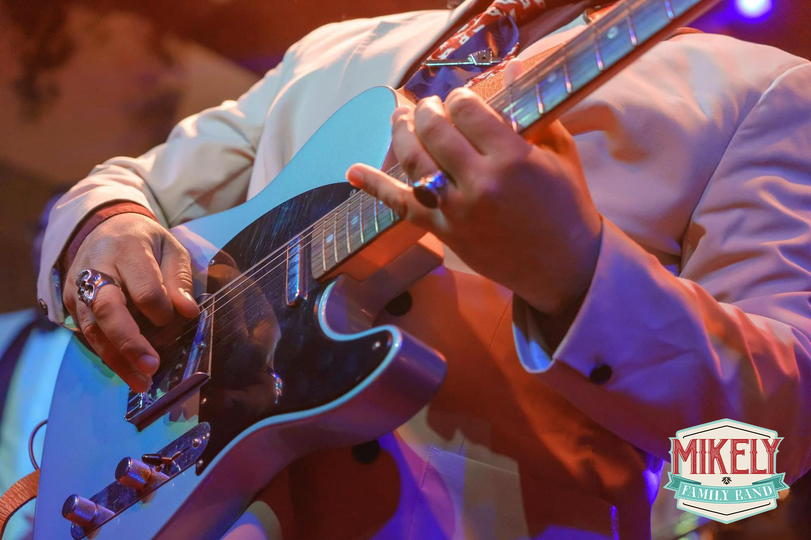 Un uomo suona una chitarra davanti a un cartello con la scritta Mikely