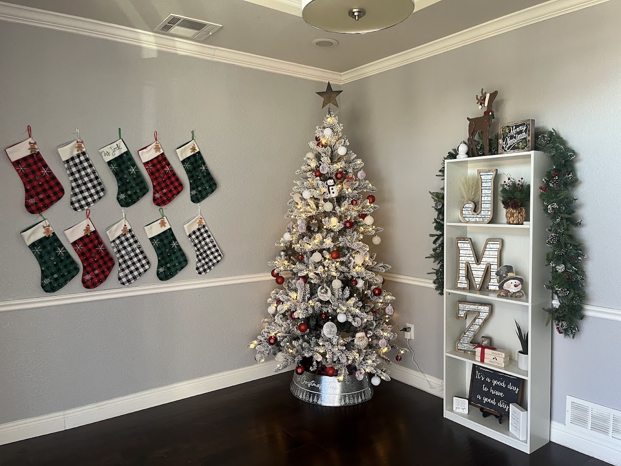 Christmas scene: stockings on wall, decorated tree, white shelving with decor, and garland.