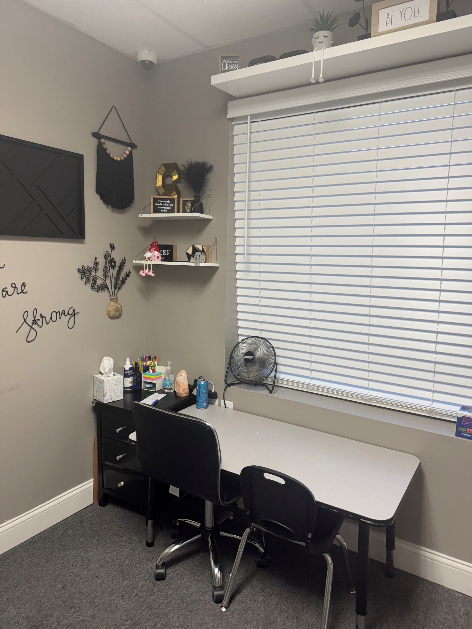A small office with a desk, shelves, and a window with blinds. Gray walls, carpet, and a desk chair.