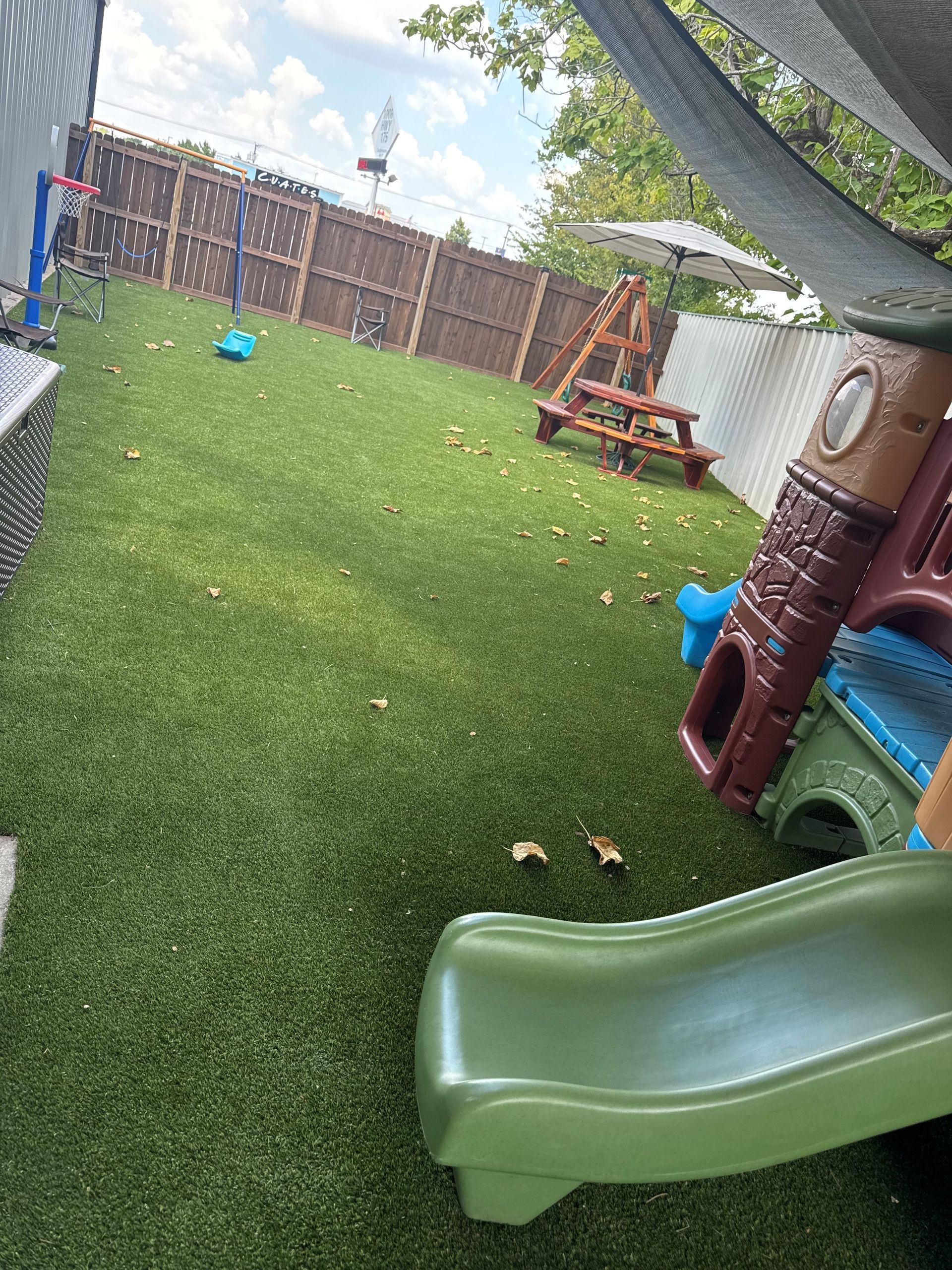 Playground with artificial turf, slide, picnic table, and fence.