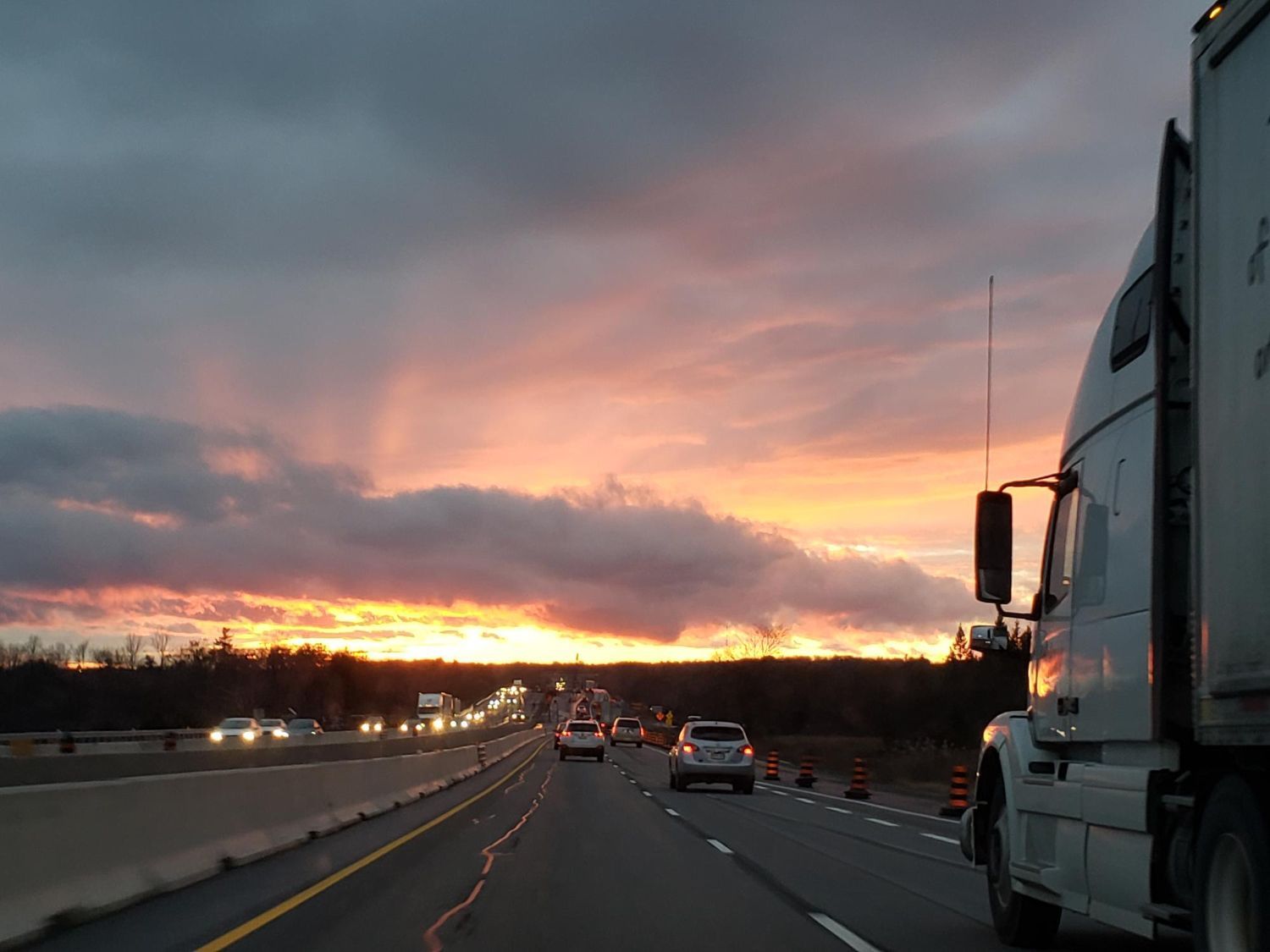 Sunset over a highway with cars and a semi-truck; orange and gray sky.