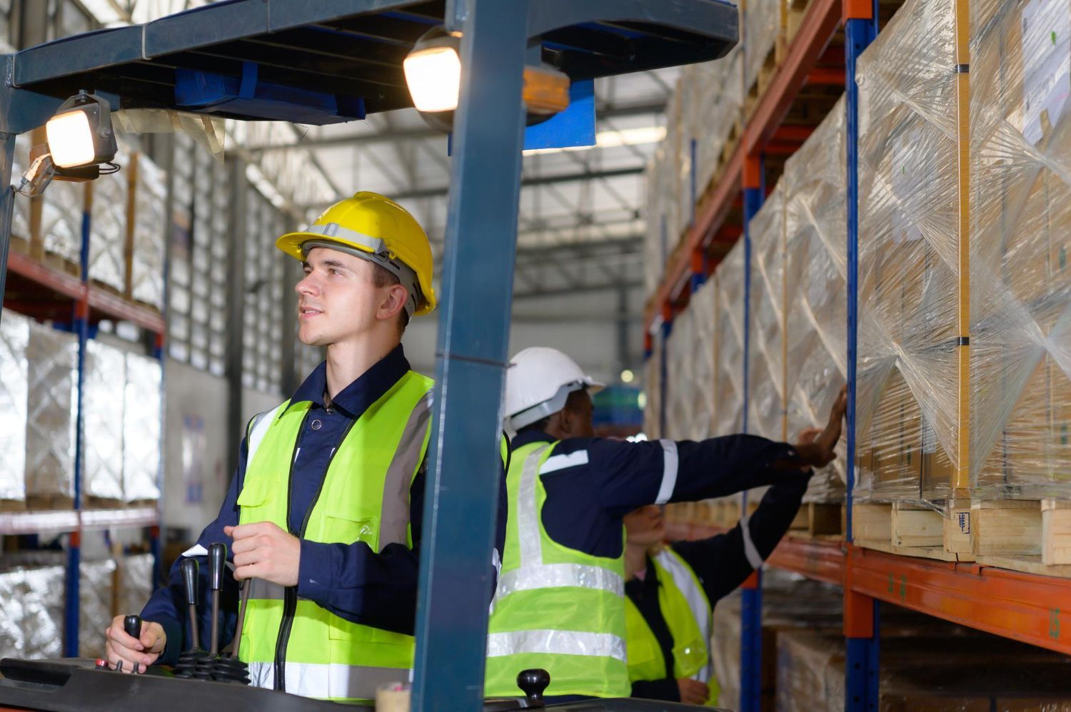 Warehouse workers operating forklift, loading pallets on shelves.