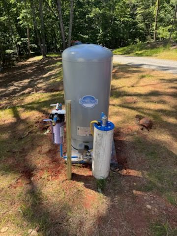 A large water tank is sitting on top of a dirt field next to a road.