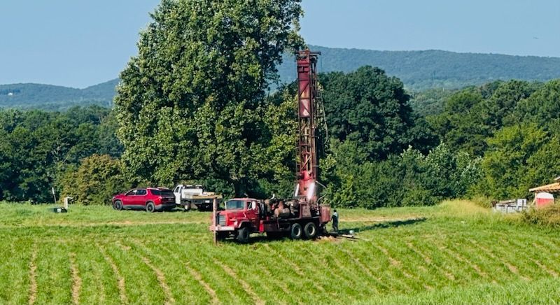 A red truck is driving through a grassy field.