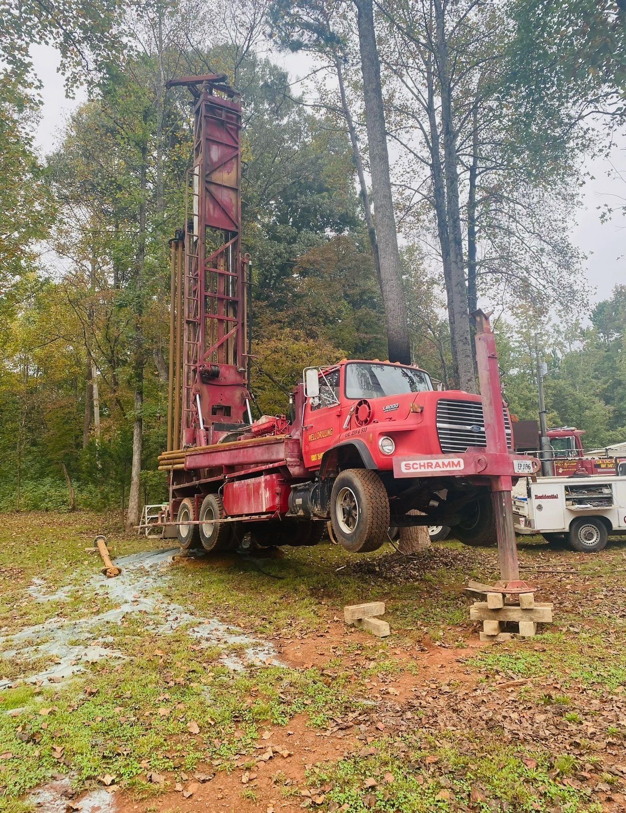A red truck is parked in a field next to a tree.