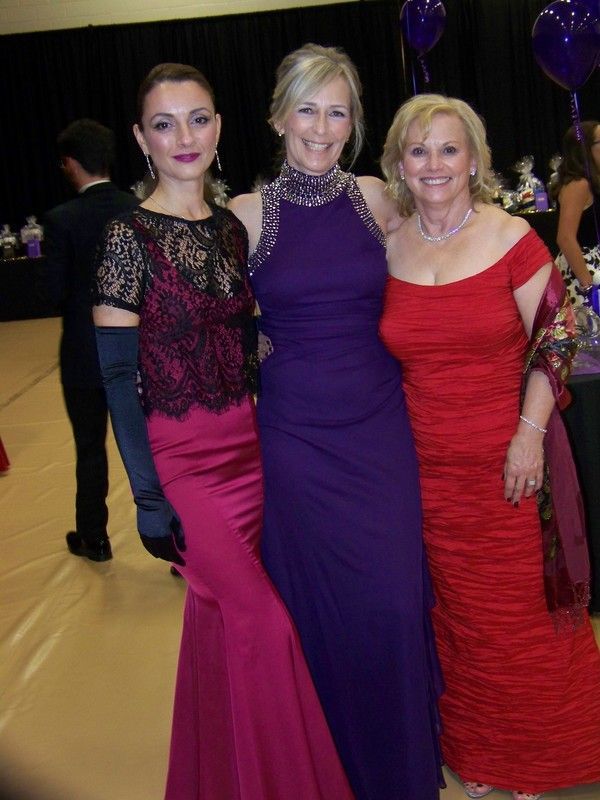 Three women in formal gowns pose together at an event.