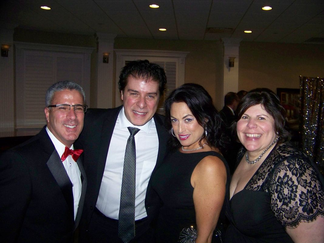 Four people smiling, posing together at an event. Man in a tuxedo with a red bow tie.