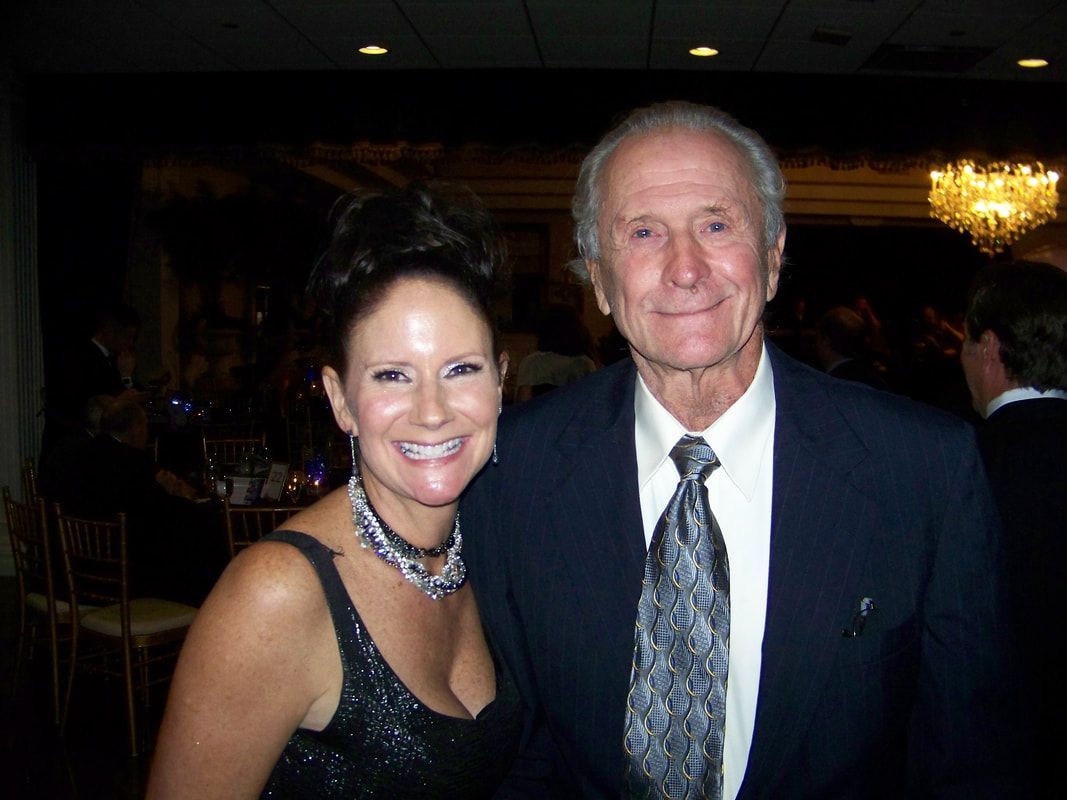 Woman in evening gown smiles next to older man in suit at a formal event.