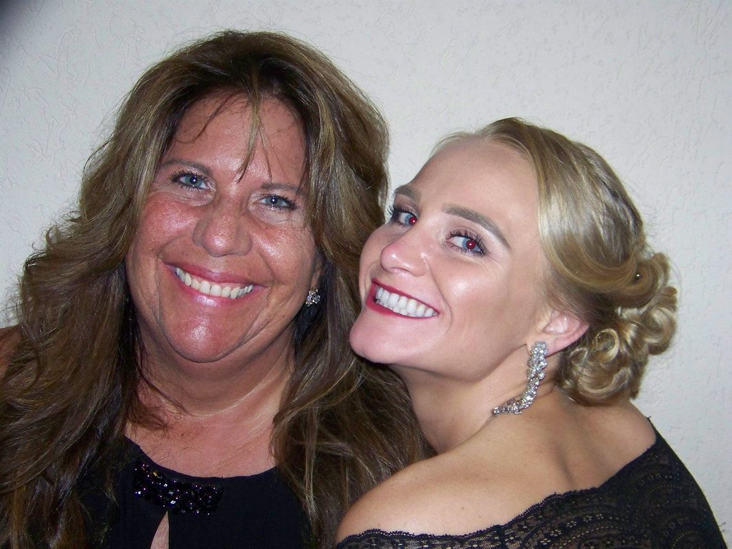 Two smiling women pose close together; one with long brown hair, the other with a formal updo.