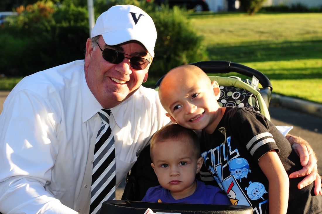 Man in white hat and sunglasses smiles with two children outdoors.