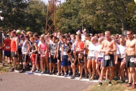 Runners at starting line of race. Outdoors, sunny. Ready to begin, some with bibs.