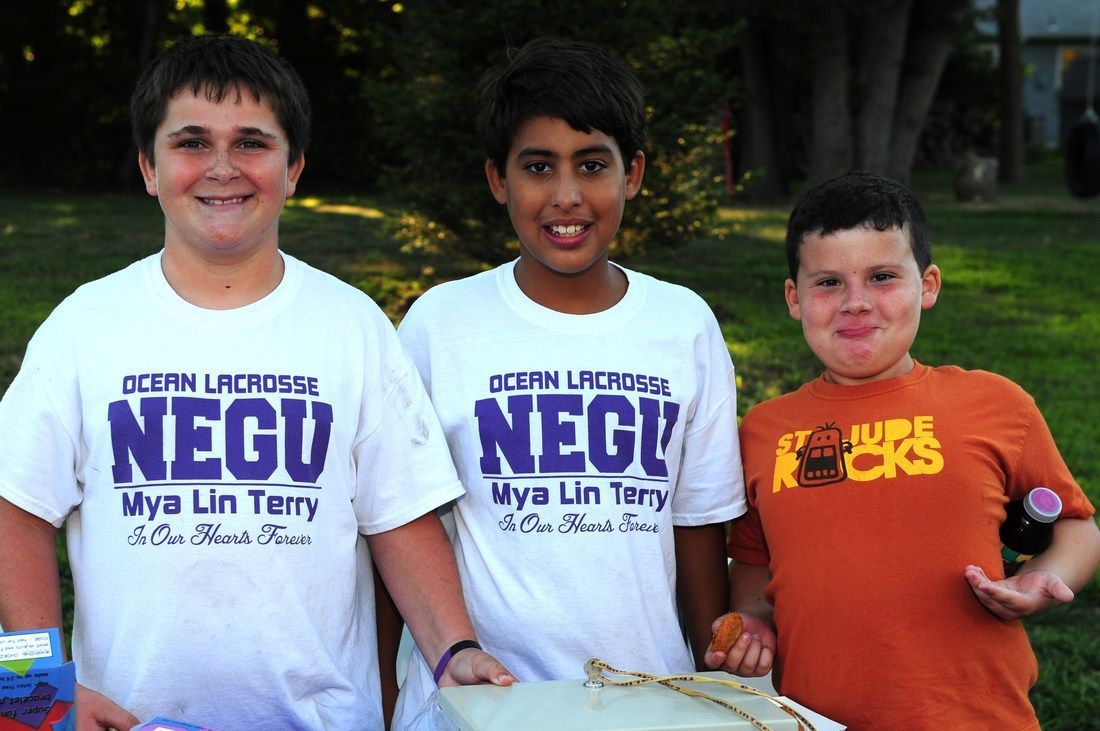 Three boys wearing t-shirts, posing outside. One boy in an orange shirt. All smiling.