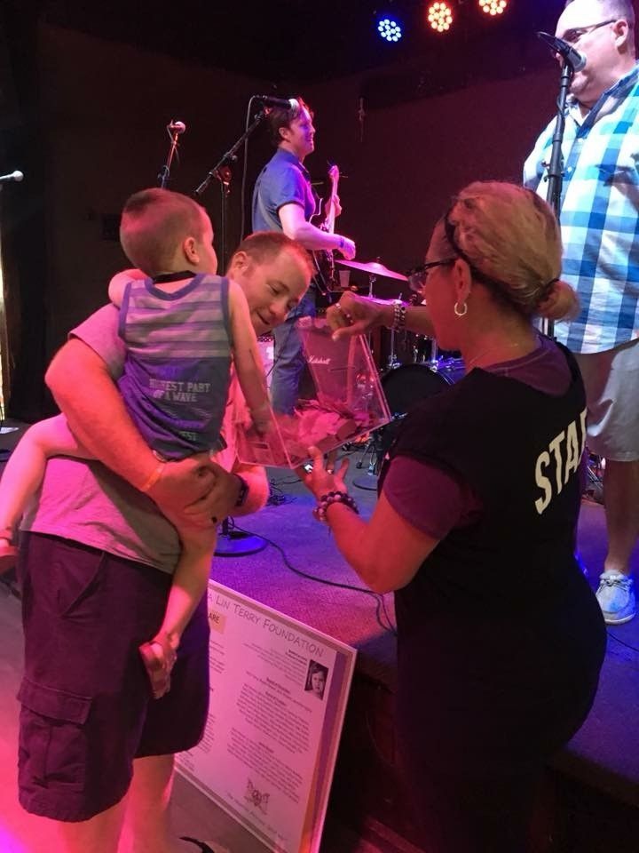 A person holding a child is given an award by a staff member on stage with a band.