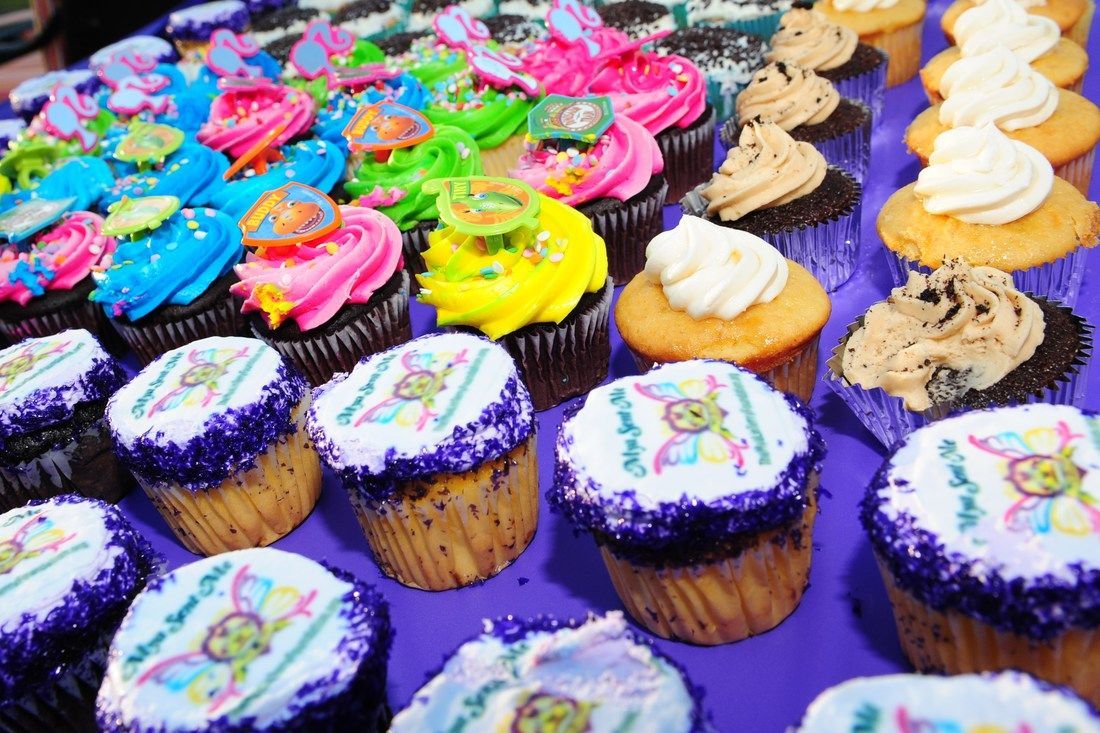 Cupcakes with colorful frosting and decorations on a purple table.