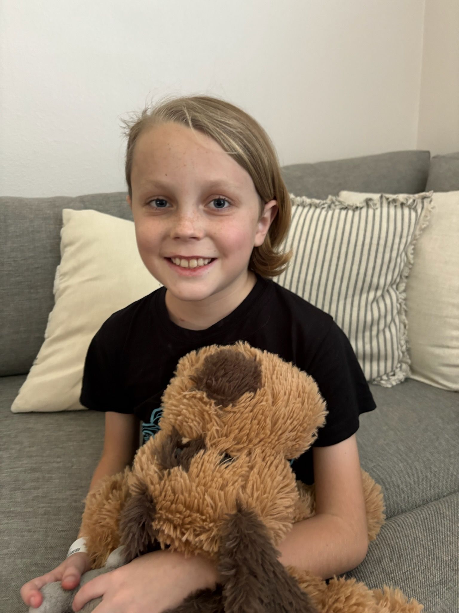 Young person in black hoodie, resting chin on hand, smiling indoors.