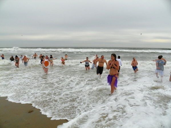 People in swimwear running into ocean waves on a cloudy day.