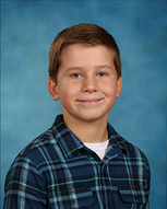 Boy with short brown hair, smiling, wearing a blue plaid shirt and white undershirt, against a blue background.
