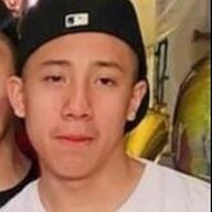 Man wearing a black baseball cap smiles, white shirt, in front of a blurred background.