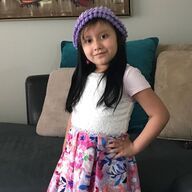 Young girl in a floral skirt and purple hat poses with her hand on her hip.