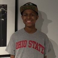 Person smiling, wearing Ohio State t-shirt and hat, standing in front of a wall.
