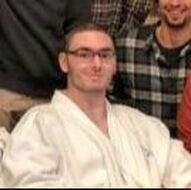 Man wearing glasses in a white karate gi, smiling in a group setting.