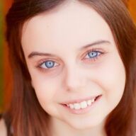 Woman with bright blue eyes smiles at the camera, with light brown hair and a warm background.