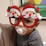 Baby wearing Santa Claus glasses, pacifier in mouth.
