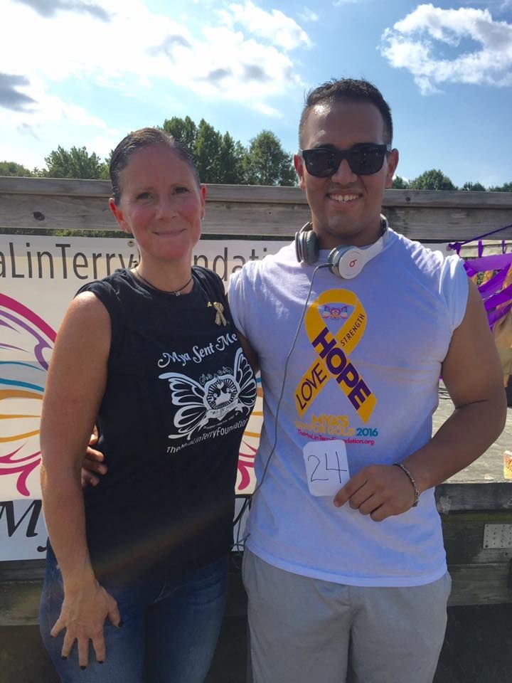 Two people smiling, posing by a sign with 