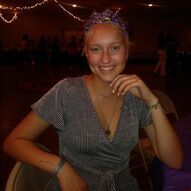Woman with blonde hair wearing a patterned headband, smiling, in a striped top; indoors, dimly lit.