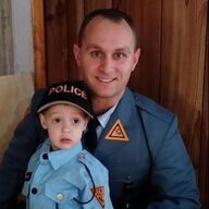 Man in uniform with a child in a police costume; they smile in front of a wood panel.
