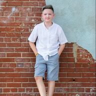 Young person in white shirt and blue shorts, leaning against a brick wall.