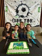 Four people with a soccer-themed cake in front of a banner that says 