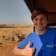 Boy giving thumbs up with two rhinos in the background, South Africa.