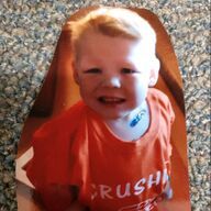 Smiling toddler with short blonde hair wearing an orange shirt. He has a blue bandage on his neck.