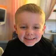 Smiling child in a black shirt, indoors, with a colorful background.