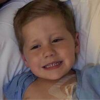 Smiling child in a blue shirt with medical tubing on his chest.