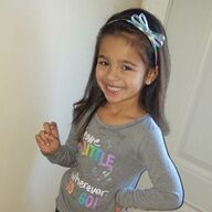 Girl smiles, wearing a grey shirt with a colorful graphic and a light blue headband.