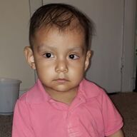 A young child with brown eyes wearing a pink collared shirt.