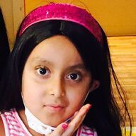 Girl with dark hair and a pink sequined headband, posing with hand near her face.