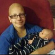 Woman in glasses and blue shirt holding a baby, both looking at the camera.